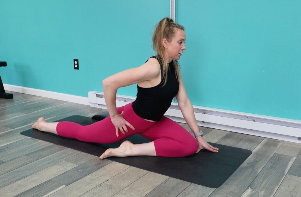 Dr. Chloe with 1 knee in front, the other leg extended back behind her on the floor in modified pigeon pose as a hip mobility for runners exercise